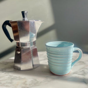 Silver espresso pot and Aqua tapered mug on a marble surface with a neutral background