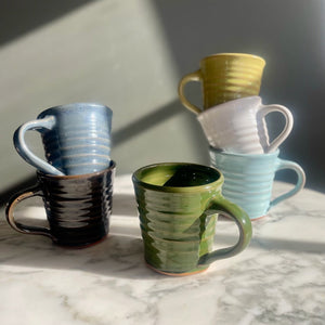 Set of colourful tapered mugs on a marble surface with a neutral background
