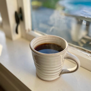 White mug with coffee on a windowsill with a blurred outdoor view