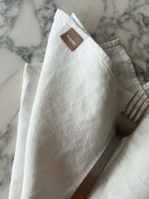 Folded white napkin with a fork on a marble surface, featuring a brand label.