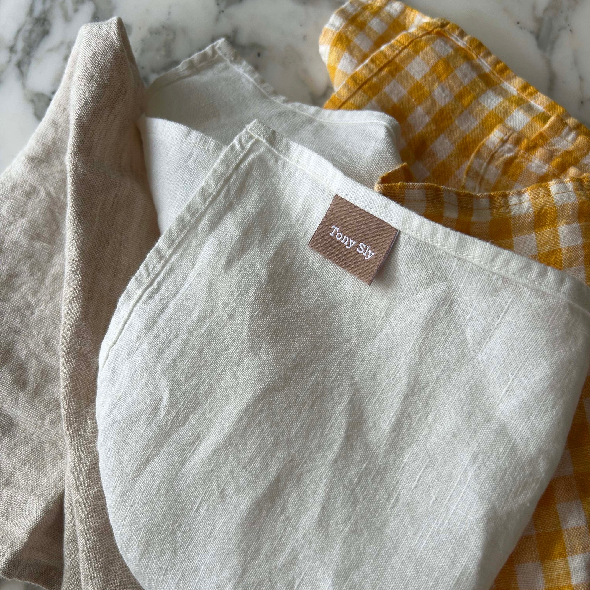 Set of folded linen napkins with a brand tag on a marble surface