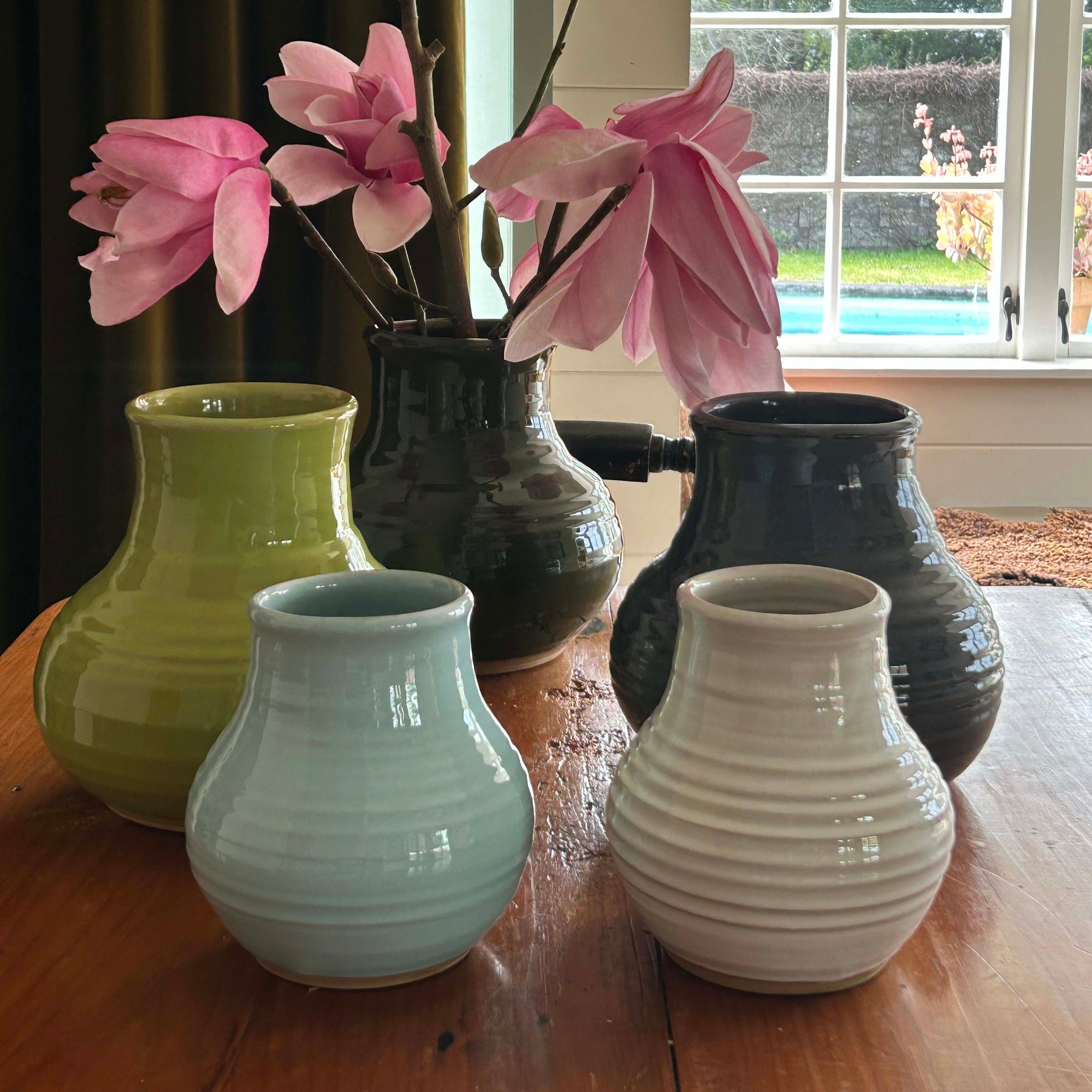 Five ceramic vases with pink flowers on a wooden surface.