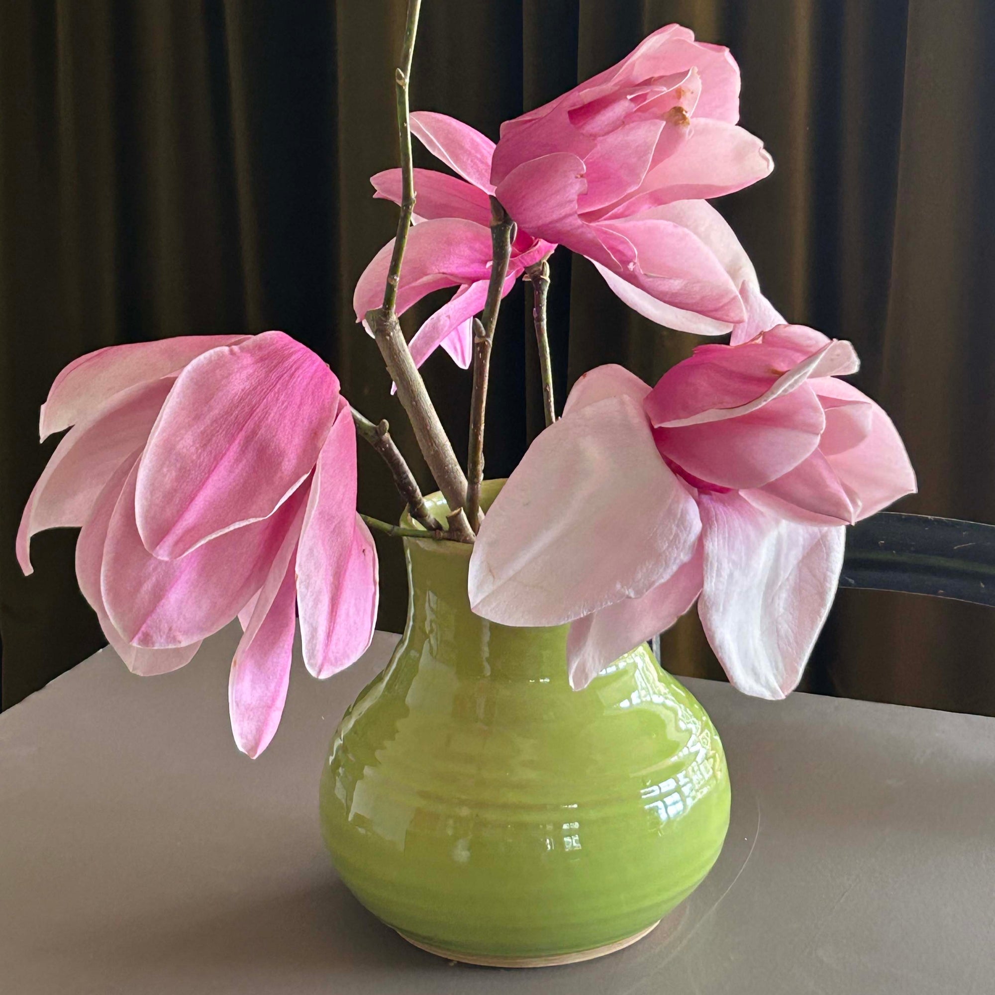Lime vase with pink flowers against a dark curtain background