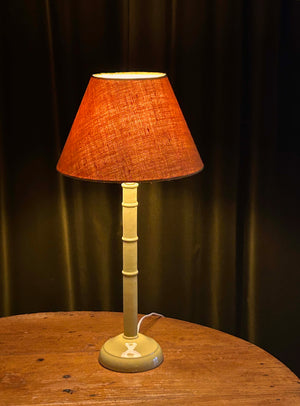 Table lamp with a terracotta lampshade on a wooden surface against a dark curtain background