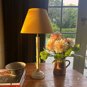 Lamp, books, and flowers on a wooden table with a window in the background