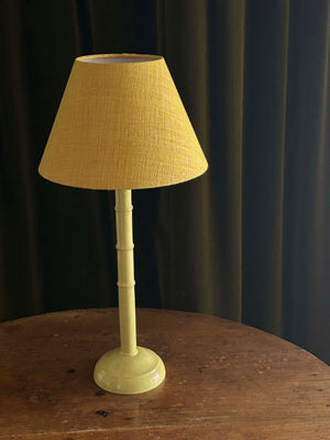 Table lamp with a yellow shade on a wooden surface against a dark curtain background