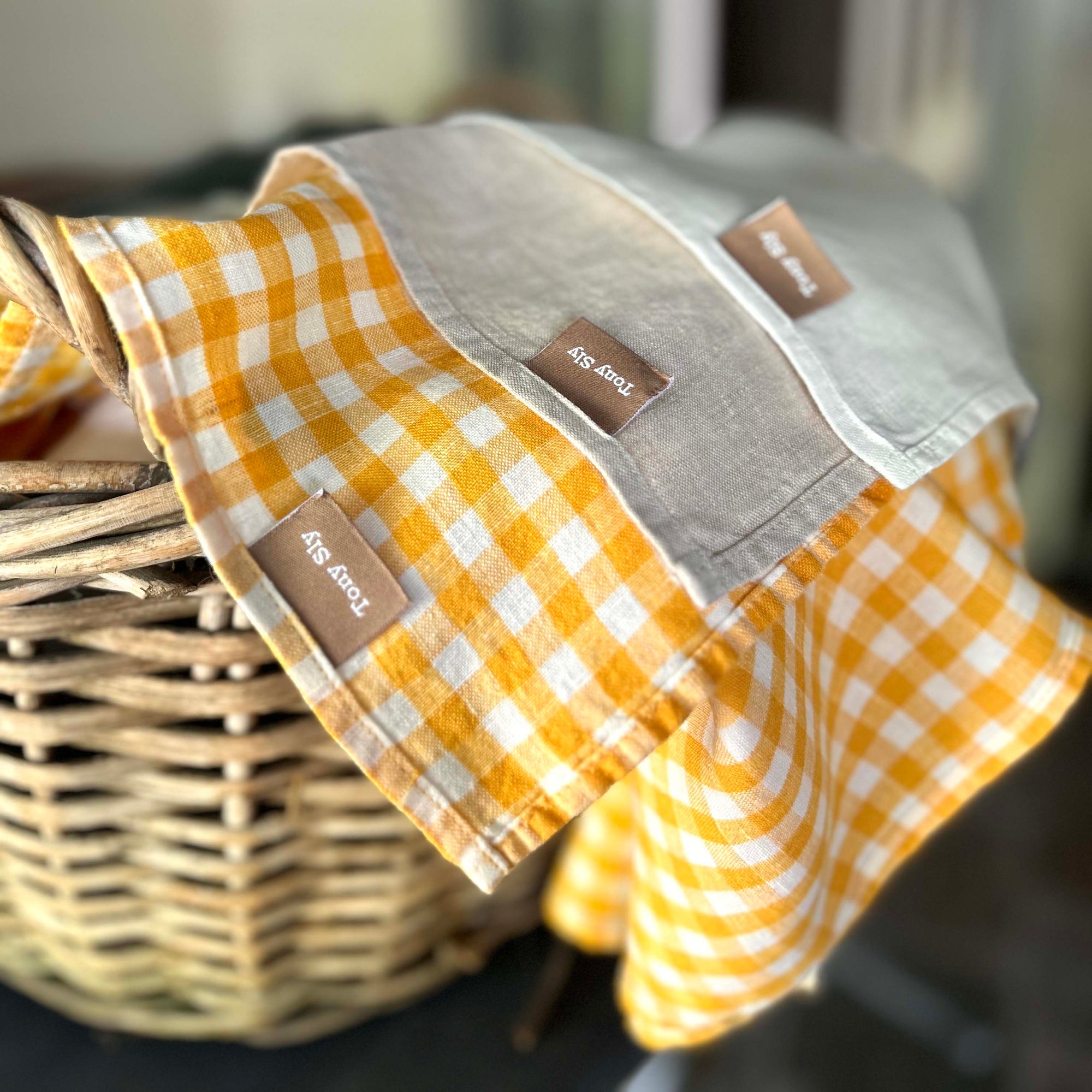 Three folded napkins in yellow check, natural, and white on a metallic surface.